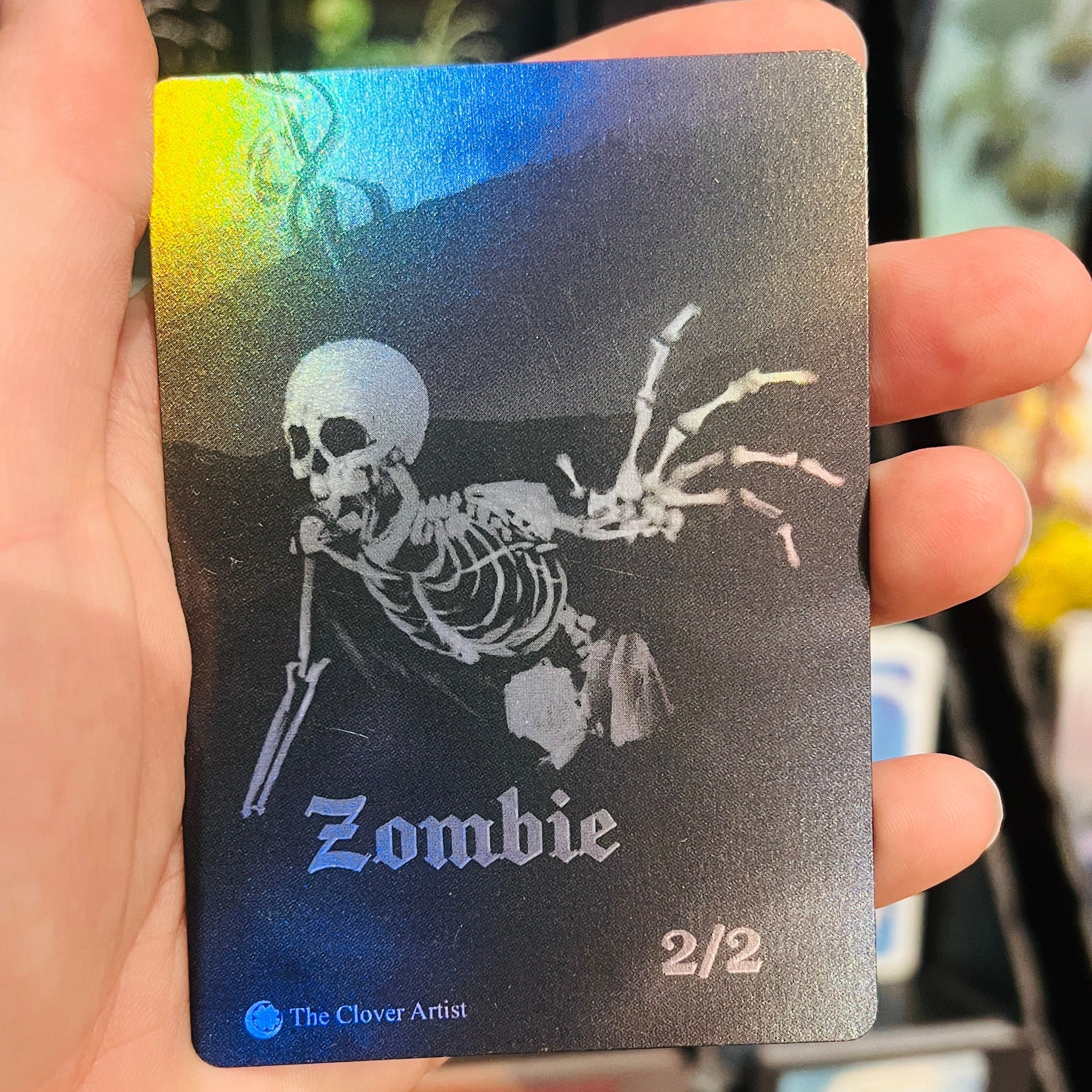 Hand holding a collectible card with a skeleton design labeled 'Zombie' against a blurred background.