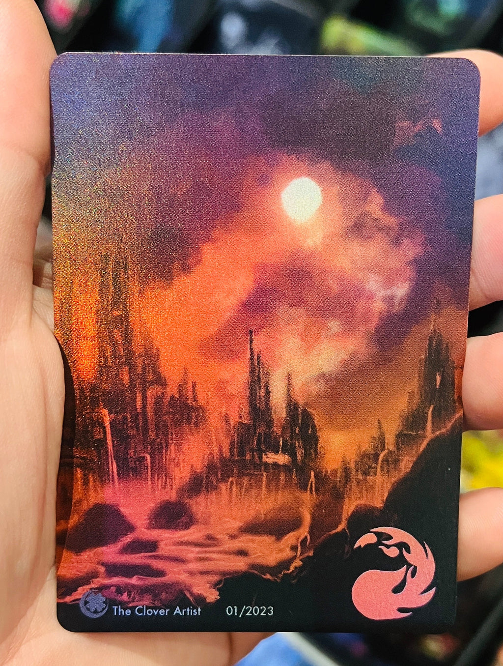Hand holding a collectible card with a fantasy scene and logo.