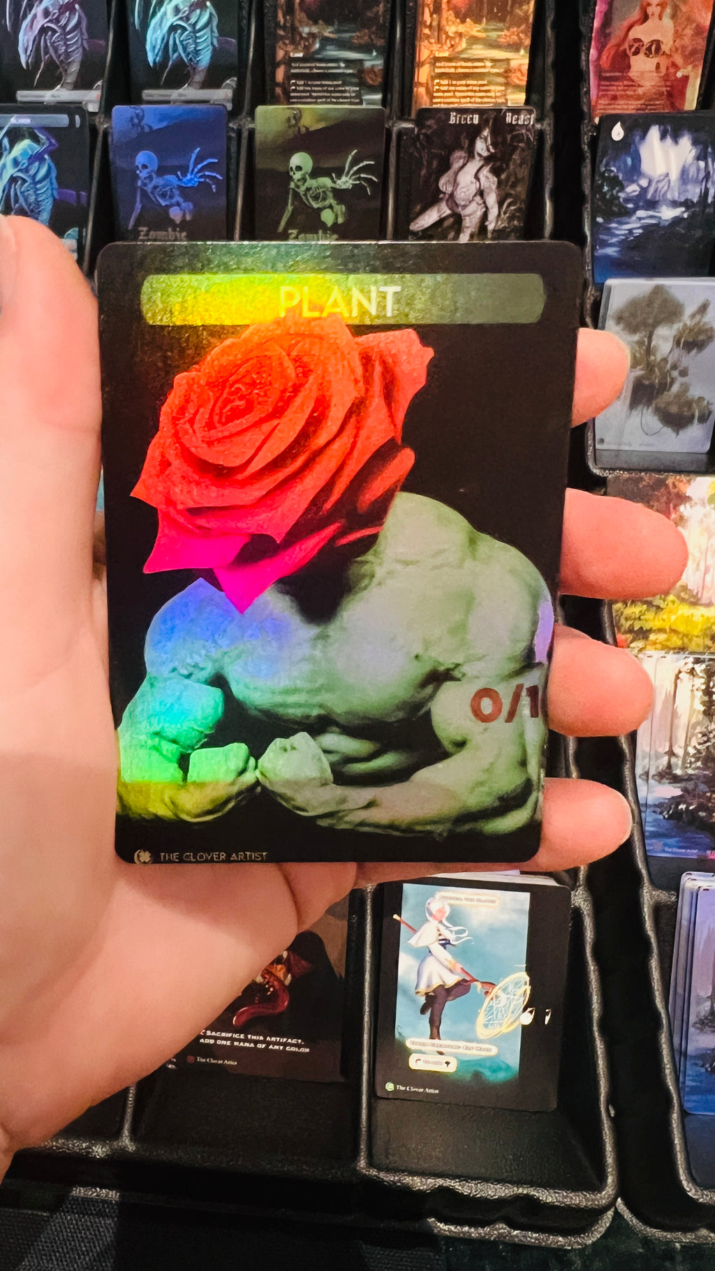Hand holding a card with a colorful design of a muscular figure and rose, surrounded by other similar cards.