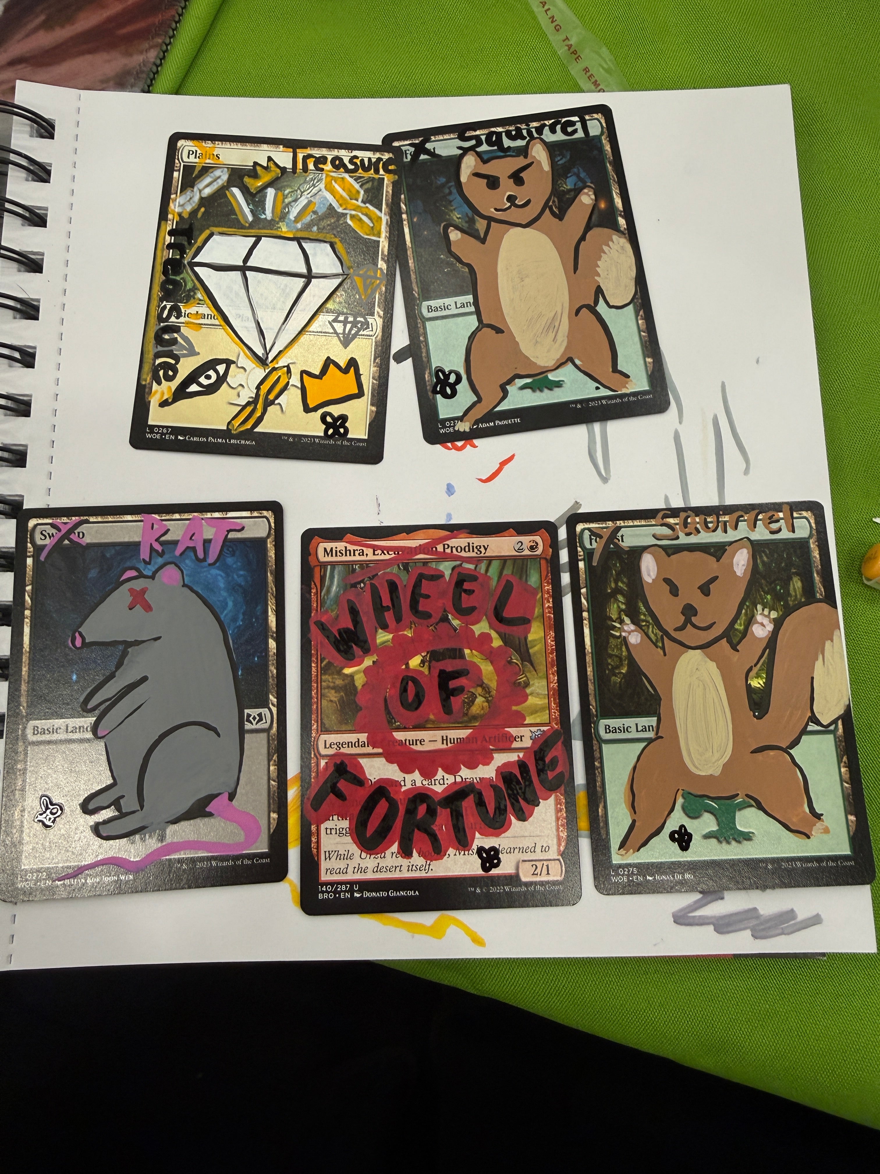 Five illustrated trading cards with handwritten notes and doodles, arranged on a white spiral notebook page over a green surface.