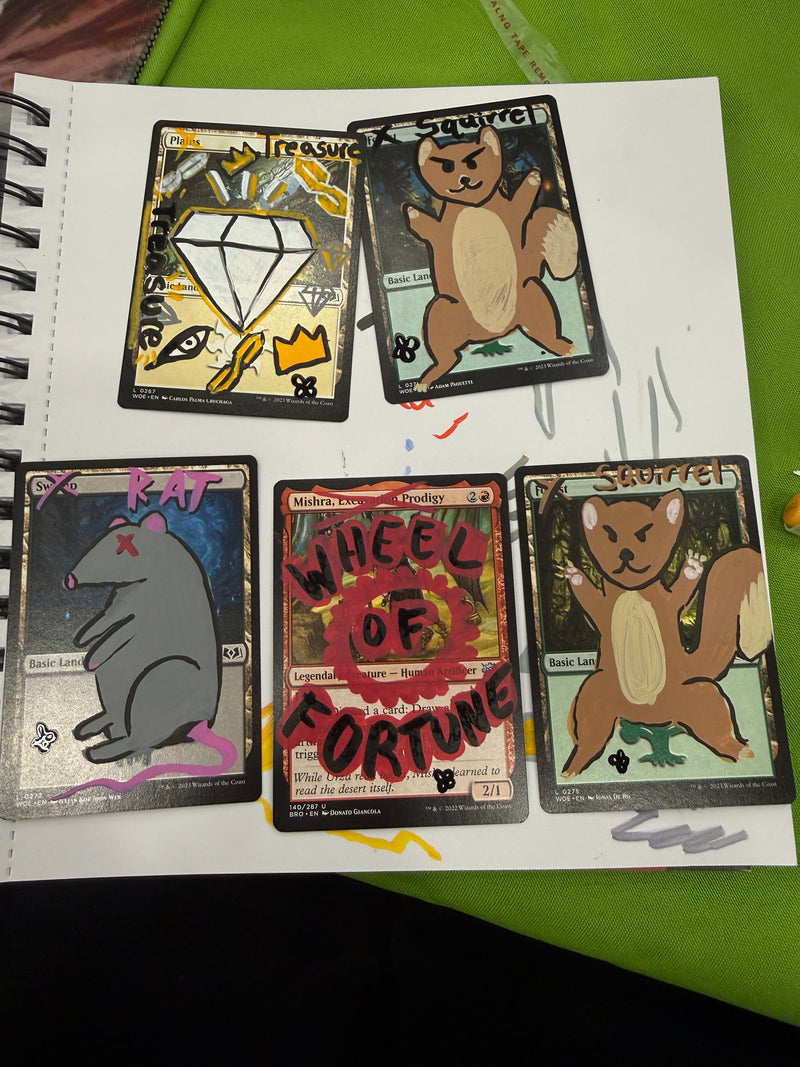 Five illustrated trading cards with handwritten notes and doodles, arranged on a white spiral notebook page over a green surface.